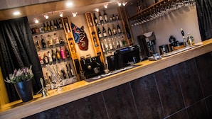 Zona de bar con estantes llenos de botellas de licores, una máquina de café y una barra con una caja registradora.