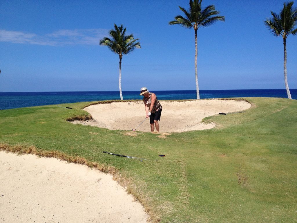 A golf course with sand bunkers, palm trees, and a clear blue sky.