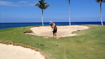A golf course with sand bunkers, palm trees, and a clear blue sky.