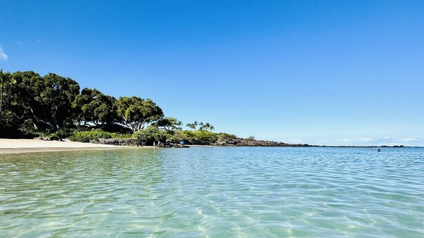 A clear beach with calm waters and a sandy shore.