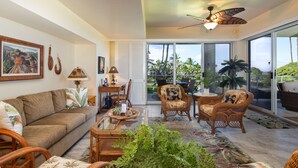 A spacious living area with a sofa, wicker chairs, a glass coffee table, and a ceiling fan.