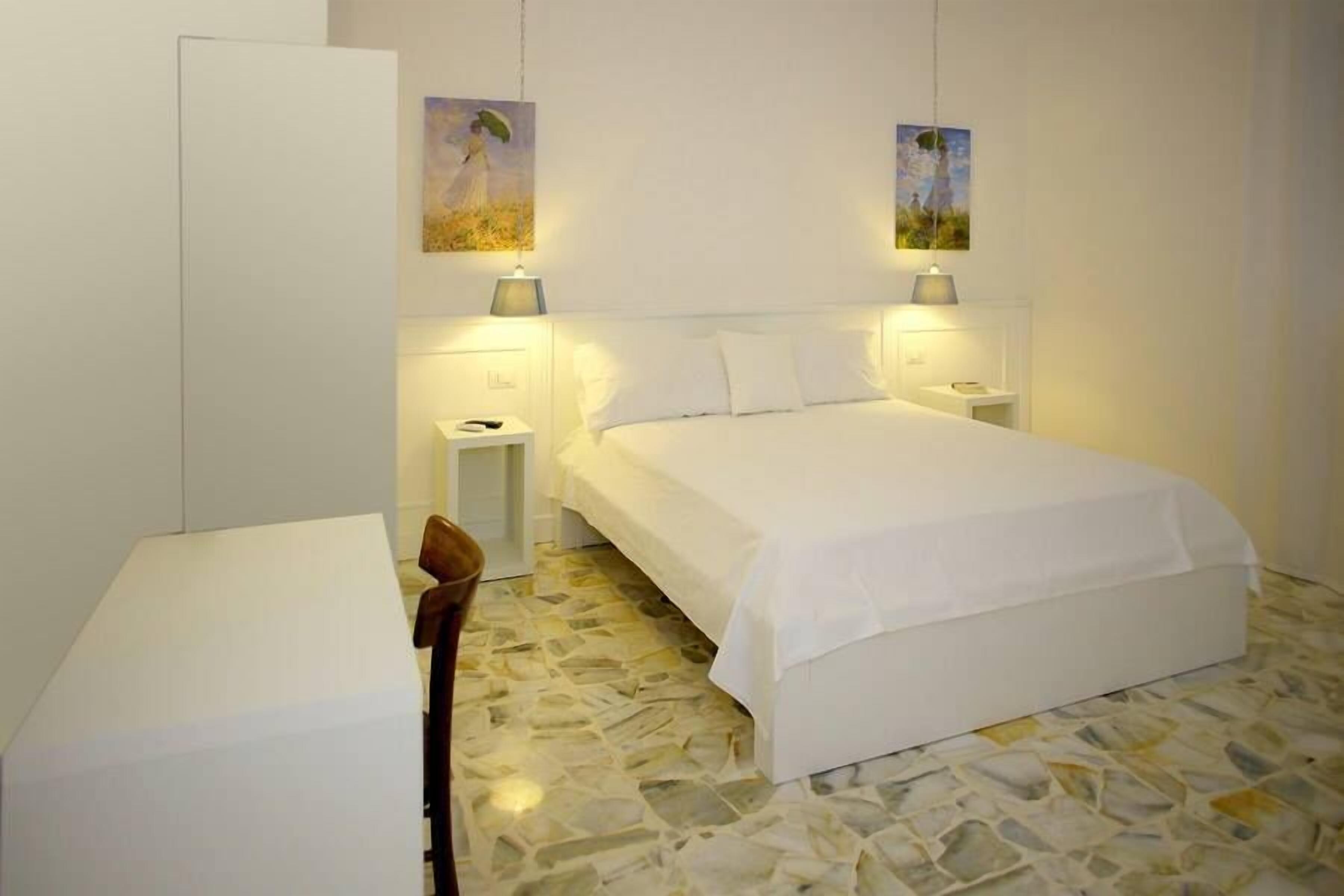 A bedroom with a bed, bedside tables, a chair, and artwork on the walls.