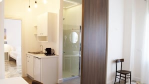 Een kleine hotelkamer met kitchenette, douche, eettafel en één stoel.