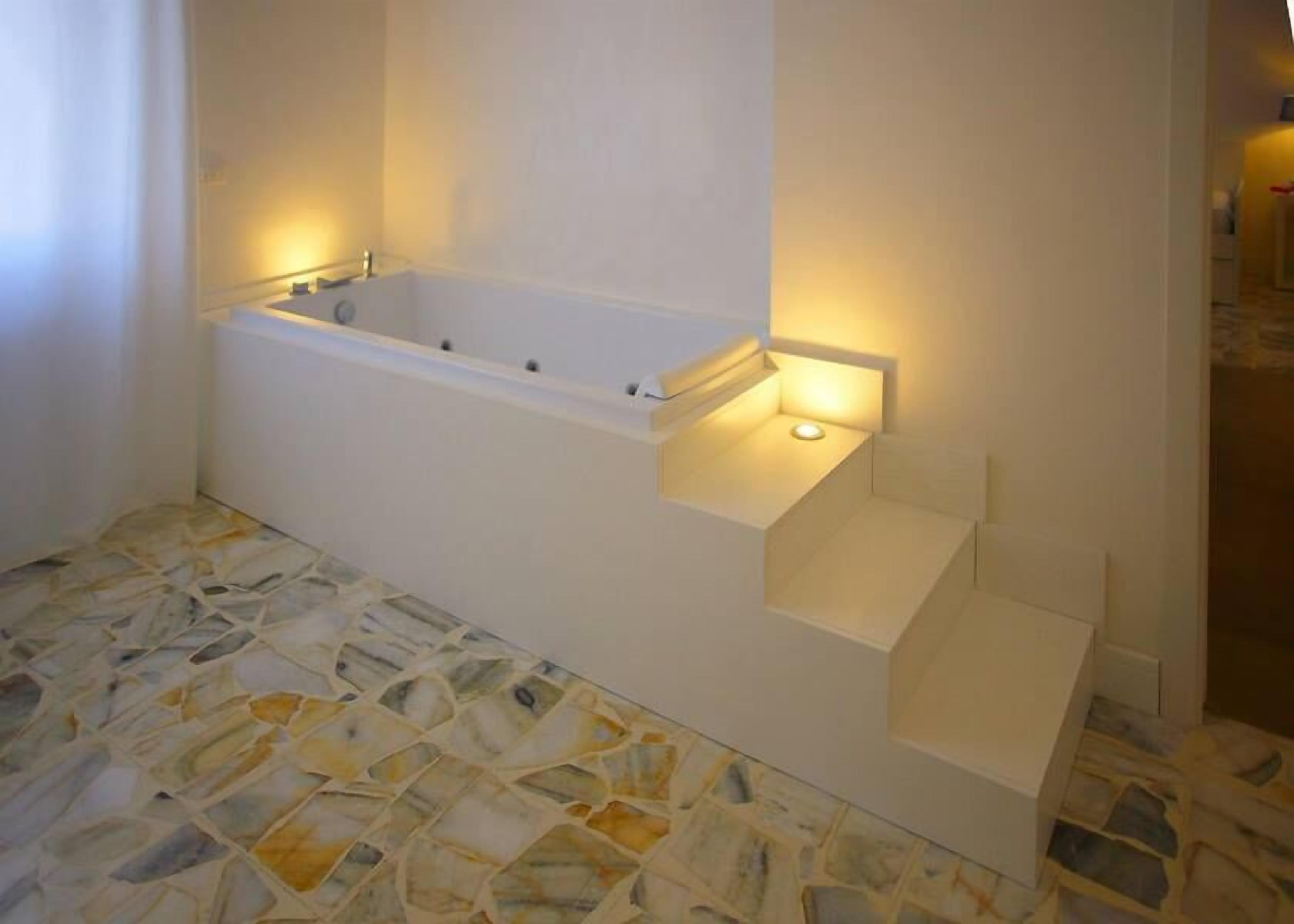 A bathroom with a white bathtub, a small sink, and a tiled floor.