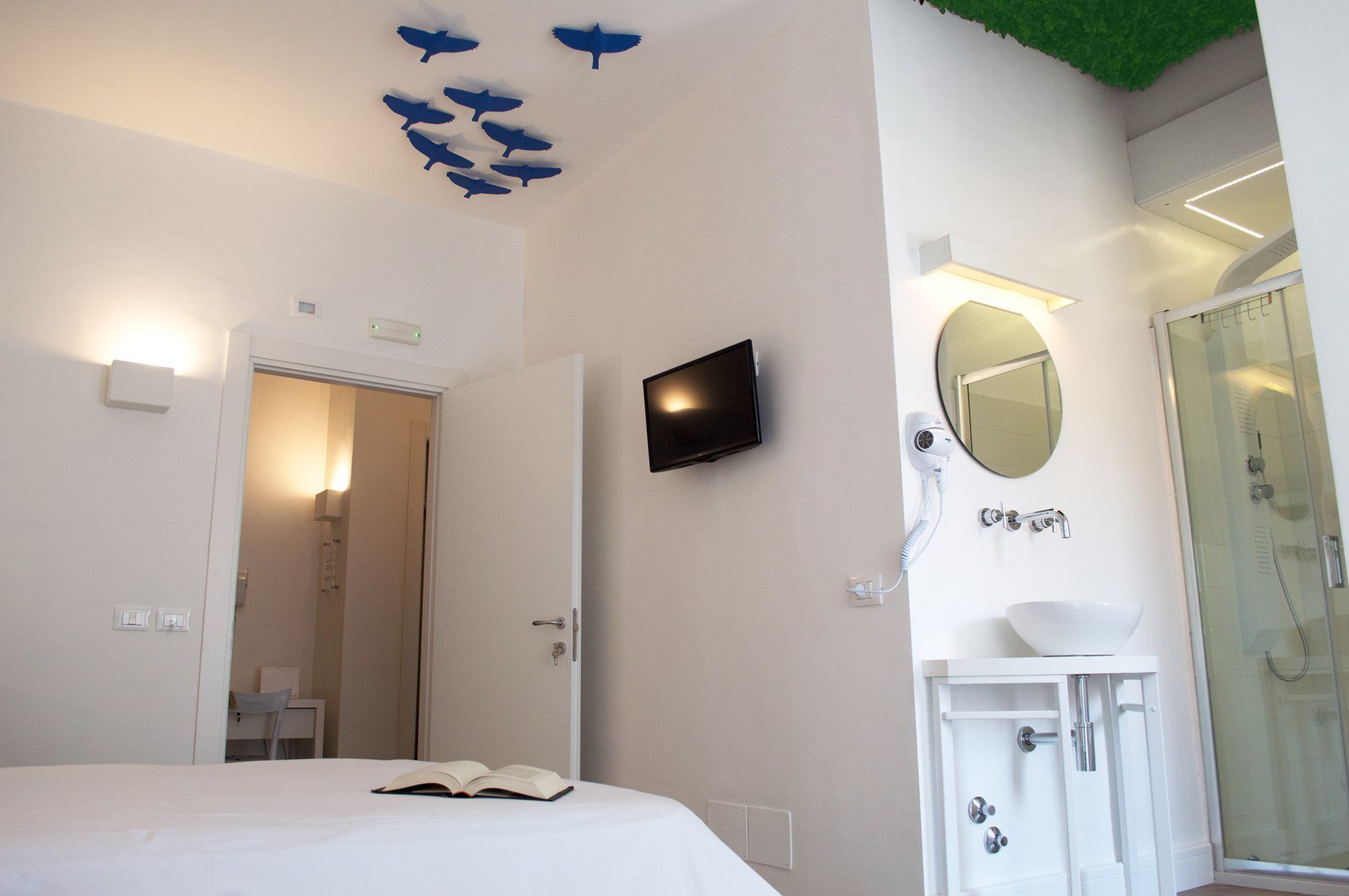 A hotel room with a bed, a TV, a bathroom with a mirror, and a shower.