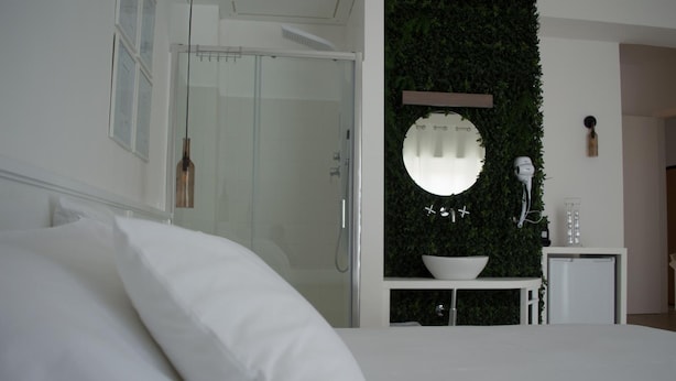 Een moderne slaapkamer met een groot bed, een douchecabine van glas, een ronde spiegel en een klein wit kastje met een schaal erbovenop.