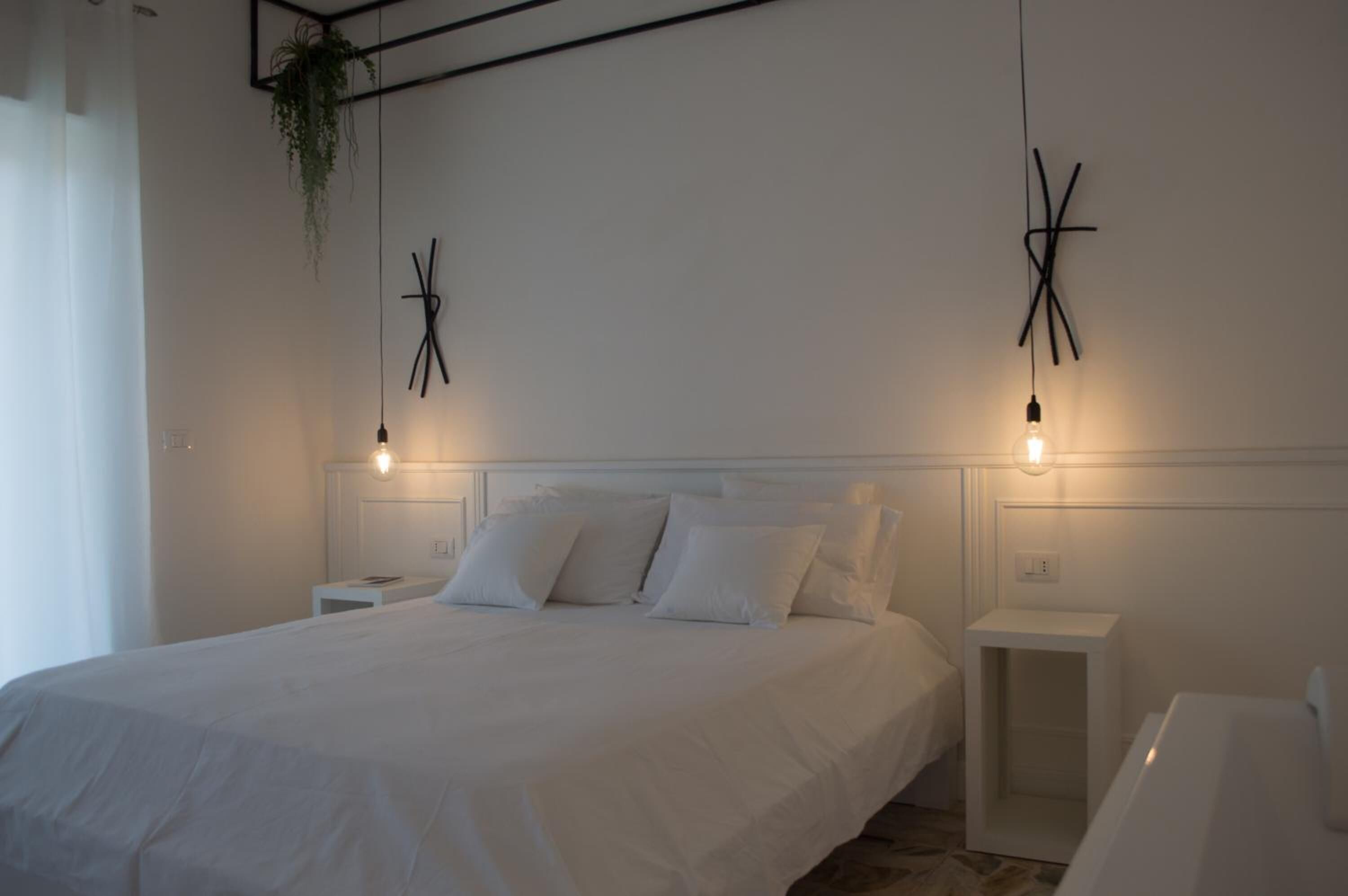 A bedroom with a large bed, bedside tables, a hanging plant, and wall-mounted light fixtures.