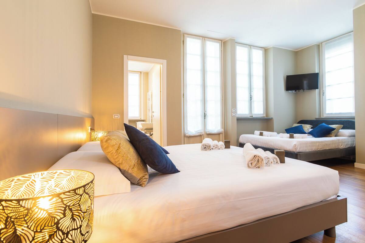 A hotel room with a large bed, a television mounted on the wall, and a window with blinds.