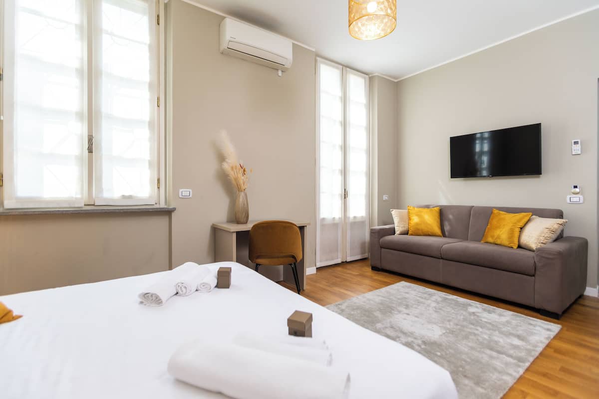 A modern hotel room with a large bed, a sofa, a TV, and a desk.