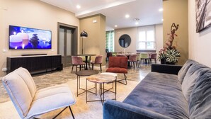A modern living room with a large flat-screen TV, comfortable seating, and a dining area with multiple chairs. - Martini Suite (Milan)