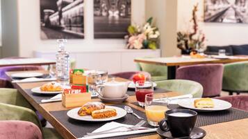 A breakfast setting with a table set for two, including plates of food, a teapot, a glass of orange juice, and a cup of coffee.