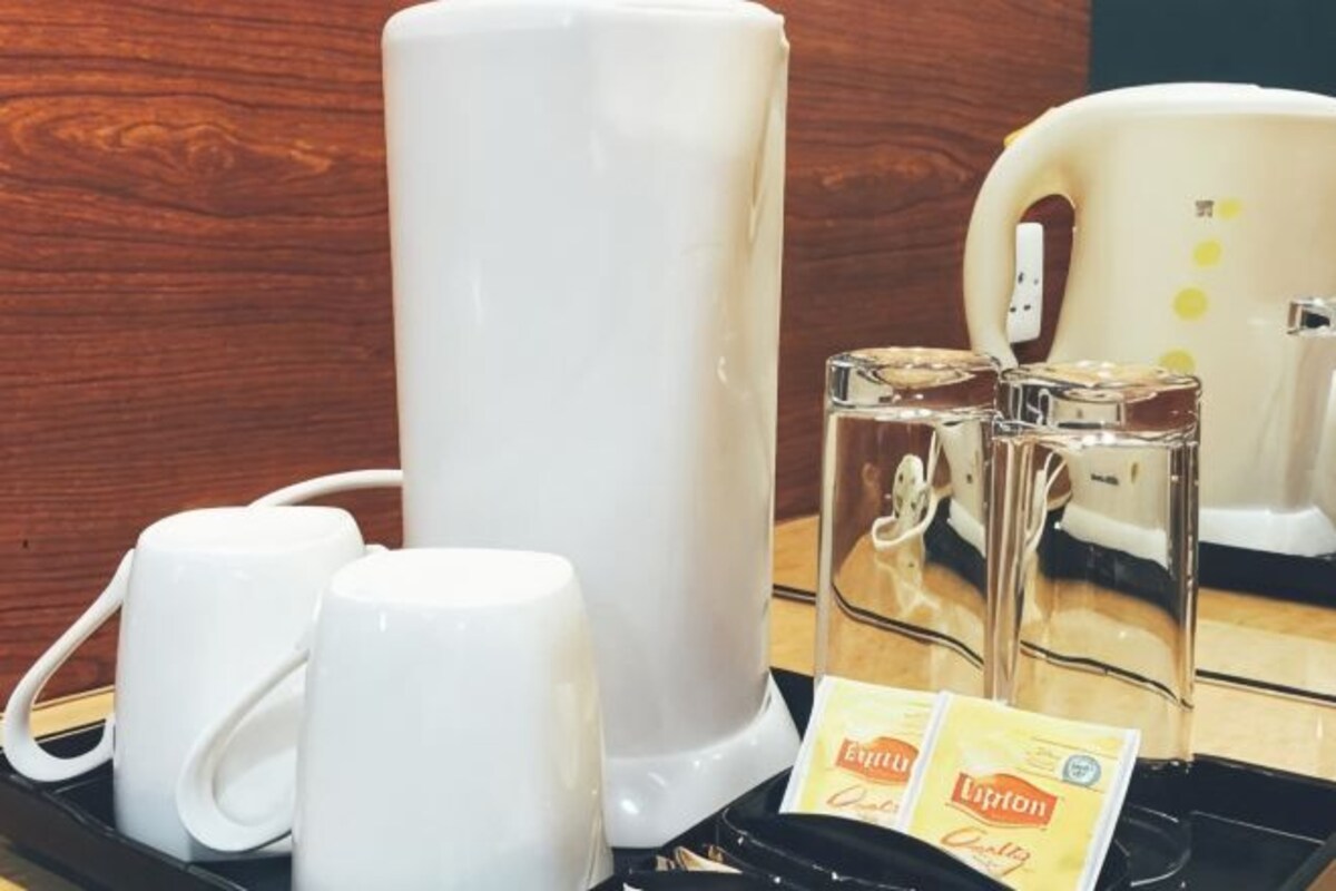 Una estación de café con una cafetera, dos tazas blancas, dos vasos de vidrio y dos sobres de té Lipton.