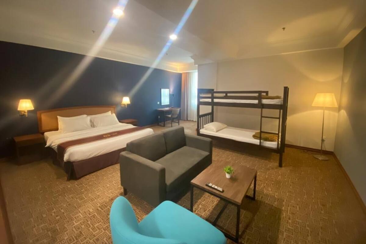 A hotel room with a bed, a sofa, a bunk bed, a small table with a plant, and a lamp.