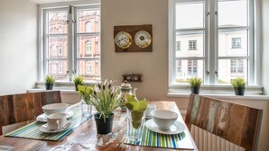 A dining area with a wooden table, chairs, and a view of buildings through large windows. - Kajüte Am Nordermarkt (Flensburg)