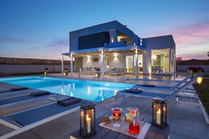 A modern house with a swimming pool, outdoor seating, and a dining area with candles. - Villa Sariva (Ispica)
