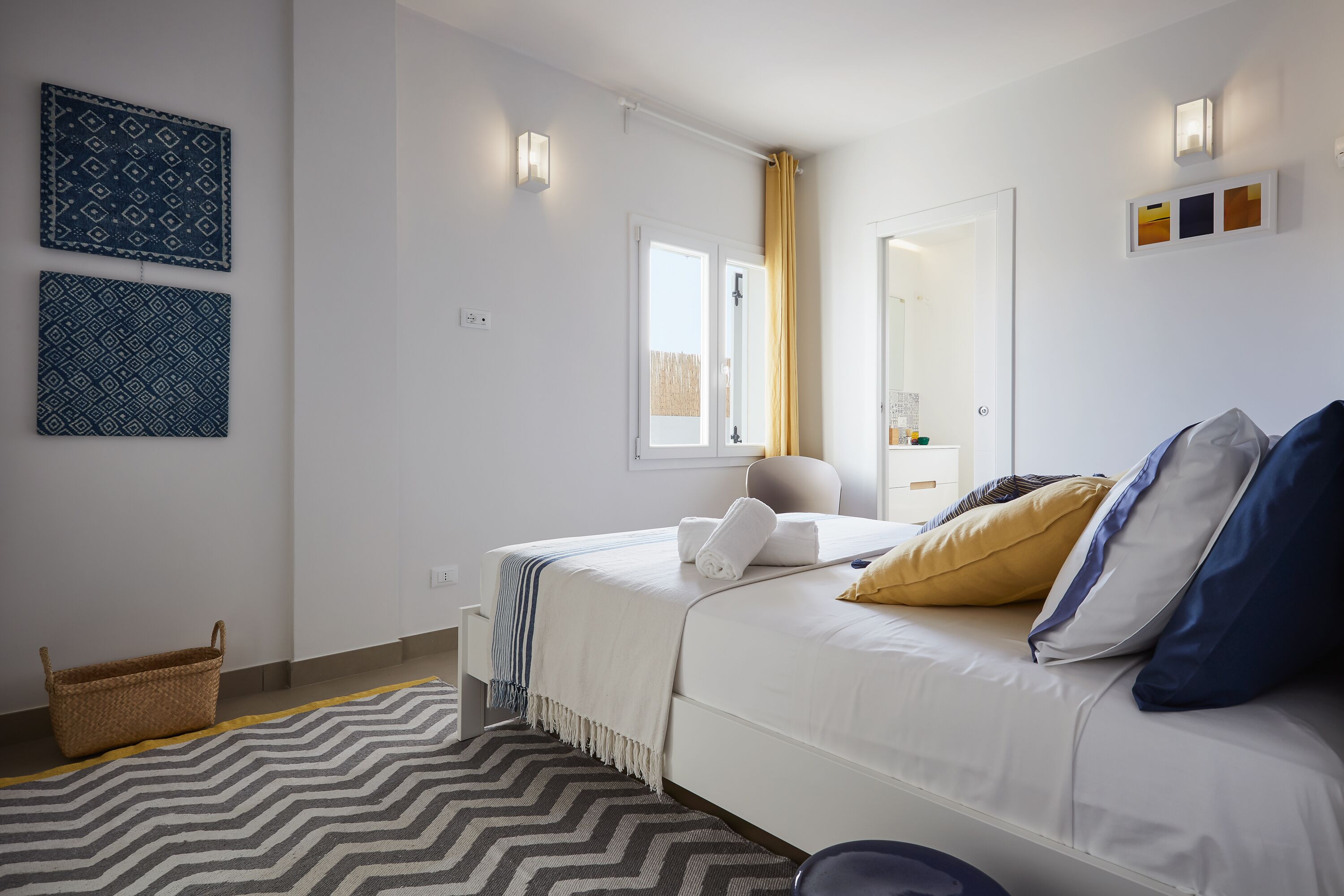 A modern bedroom with a bed, a bedside table, a mirror, and a window with curtains.
