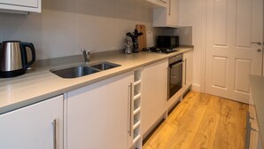 A modern kitchen with white cabinets, stainless steel appliances, and a wooden floor.