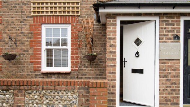 A brick building with a white door, a window with shutters, and a stone wall with pebbles.