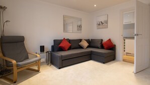 A modern living room with a grey sectional sofa, a wooden armchair, and a floor lamp.