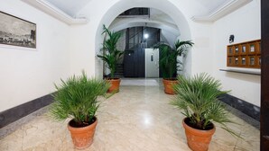 Een hal met een marmeren vloer, planten in potten, een trap en een houten kast.