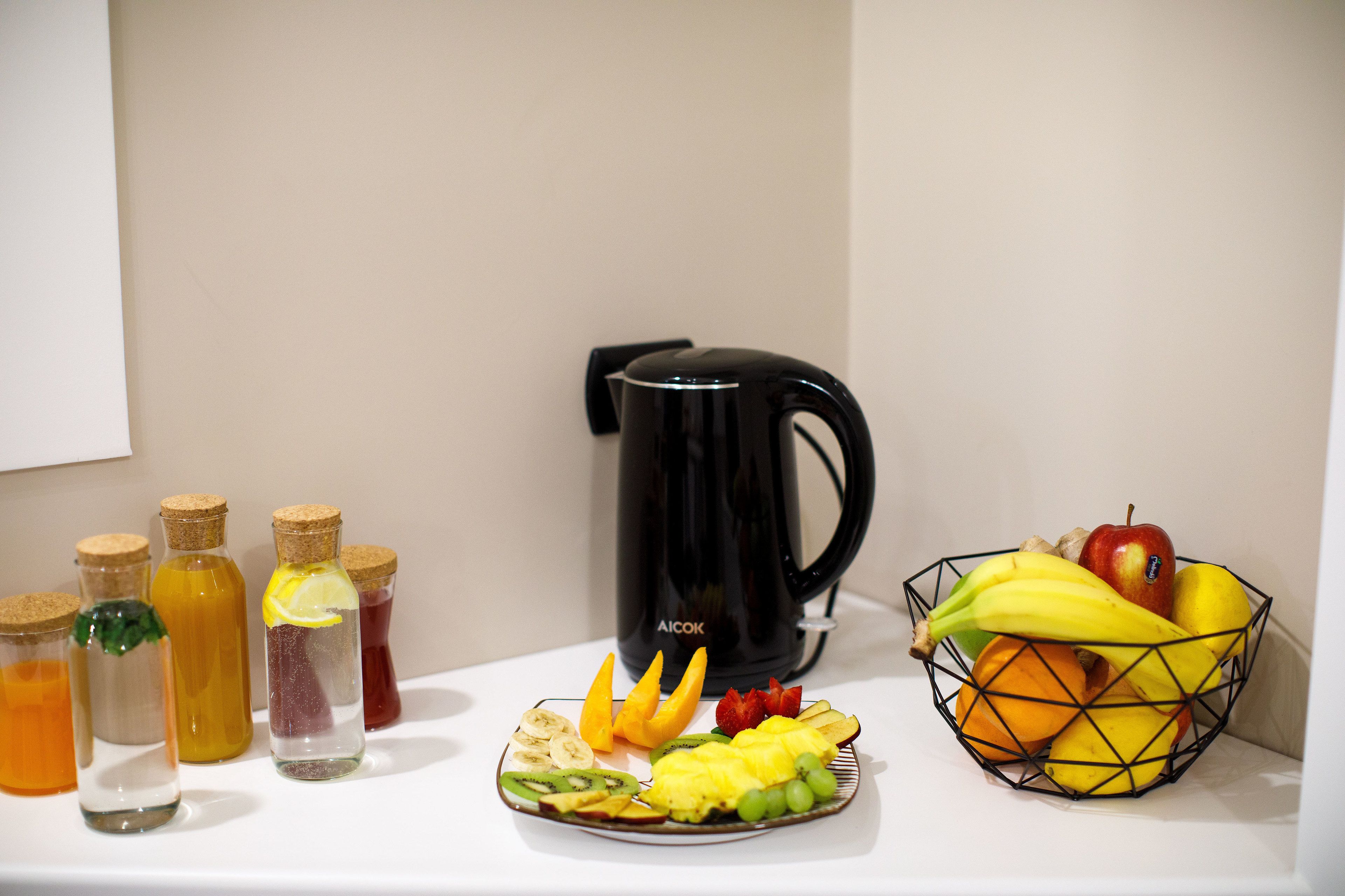 Une table avec un panier de fruits, une assiette de fruits et plusieurs bouteilles de boissons.