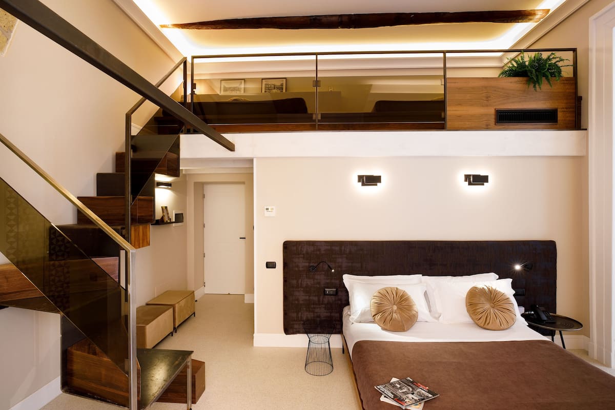 Un dormitorio moderno con una cama grande, cabecera de madera y una escalera con barandales de vidrio.