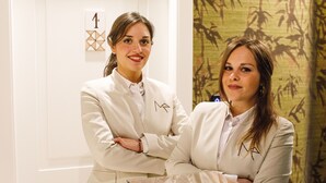 Twee personen in een professionele omgeving met een modern interieur, waaronder een glazen wand en een muur met een geometrisch patroon.