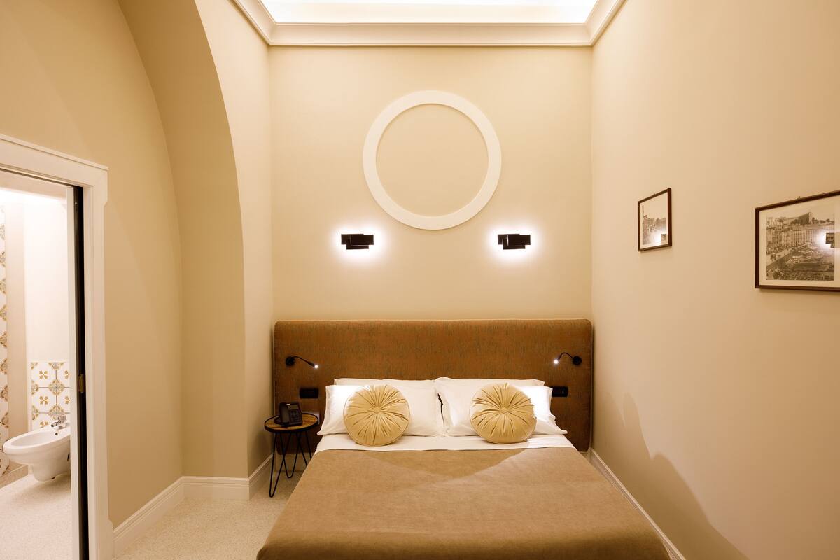 Un dormitorio con una cama grande, un espejo redondo en la pared, dos lámparas de noche y un cuadro enmarcado.