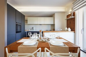 A modern kitchen with dark blue cabinets, a wooden dining table set for two, and a view of the adjacent dining area.