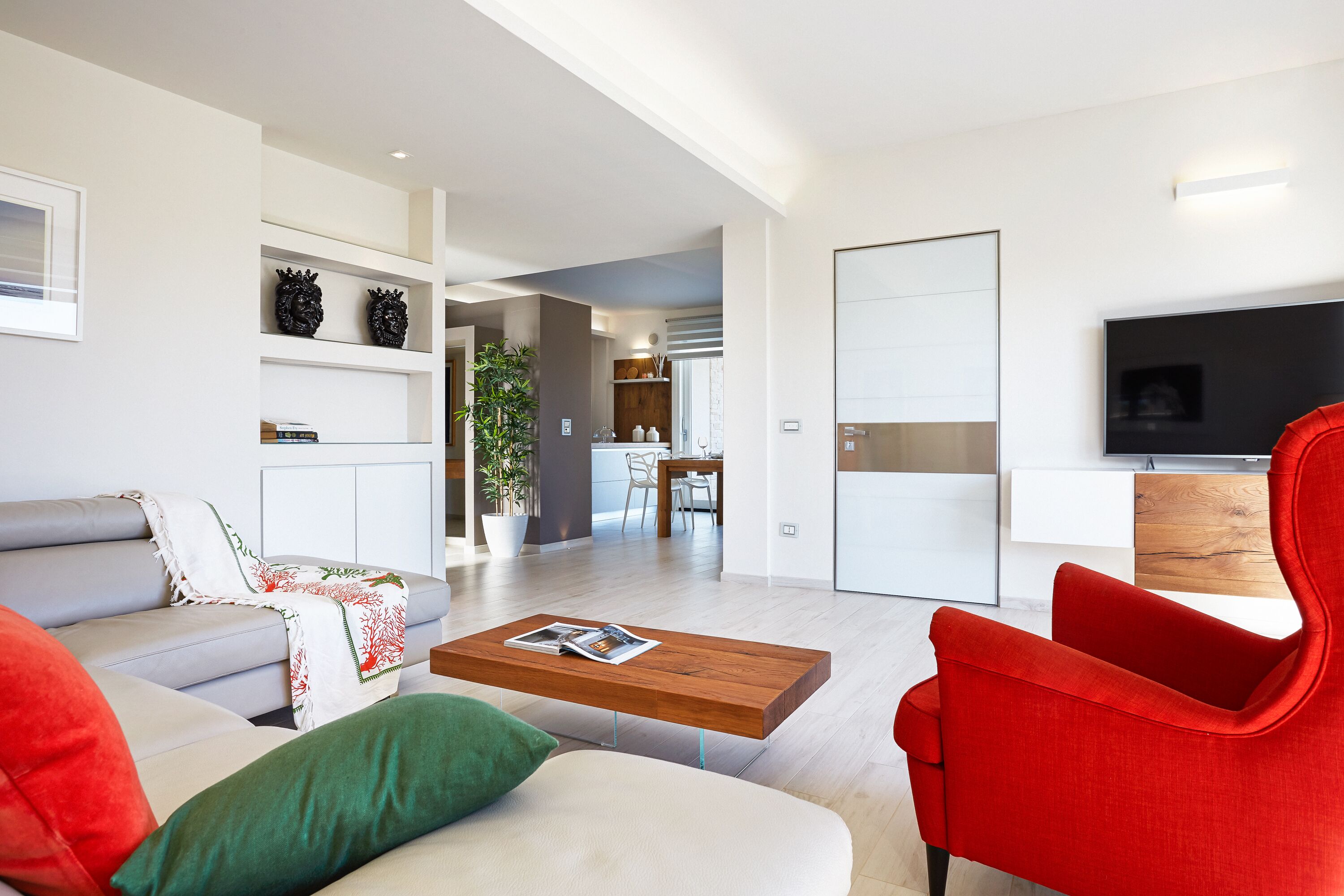 A modern living room with a sofa, a red chair, a coffee table with a magazine, and a TV on a wooden cabinet.