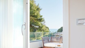 Una habitación con suelo de madera, puerta corredera de vidrio que da a un balcón exterior con mesa y sillas.