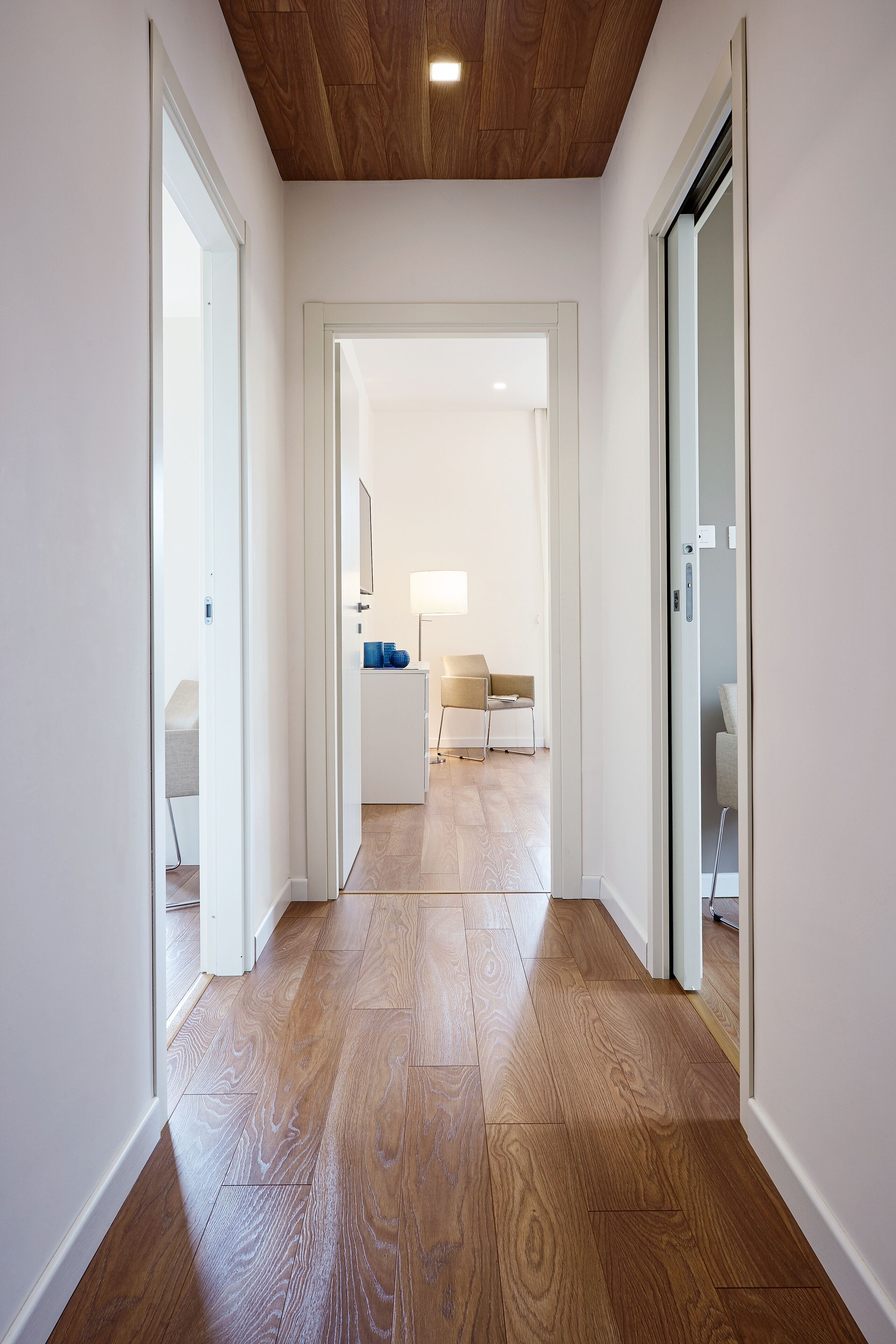 Un pasillo con suelo de madera, paredes blancas y techo con paneles de madera.