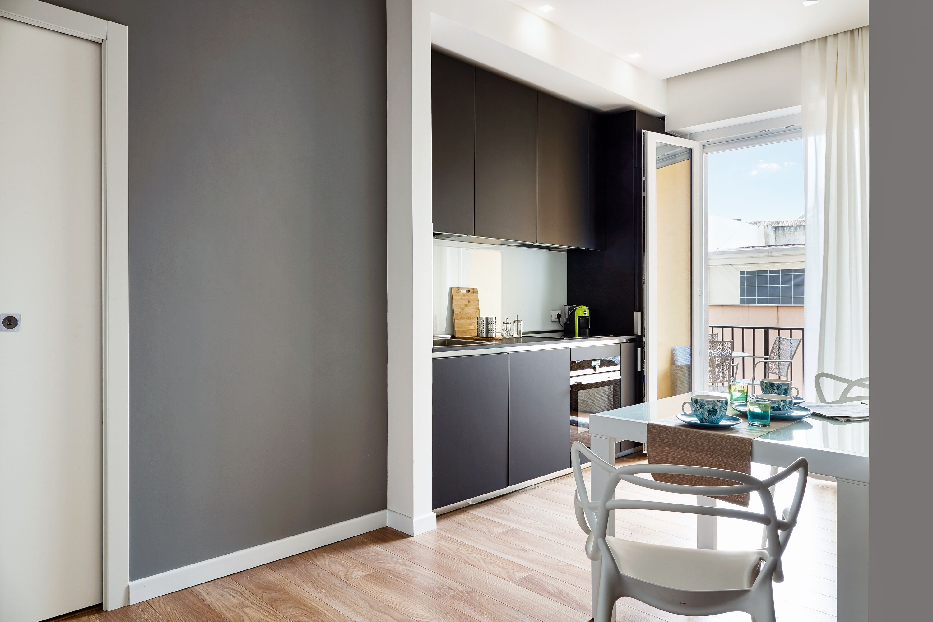 Una cocina moderna con armarios oscuros, encimera blanca y zona de comedor con mesa y sillas.