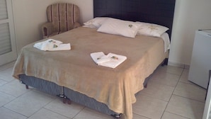 A neatly made bed with a headboard, a chair, and a small white appliance, likely a refrigerator, in a room with tiled flooring. - Vista Alegre Hotel (Ibitinga)