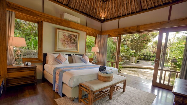 A bedroom with a large bed, wooden headboard, and a view of the garden through a sliding door. - Umah Lawas Ubud (Ubud)