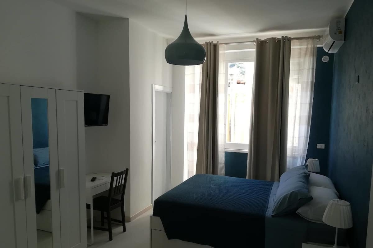 Ein Schlafzimmer mit einem Bett, einem Schreibtisch, einem Stuhl, einem Fernseher und einem Fenster mit Vorhängen.