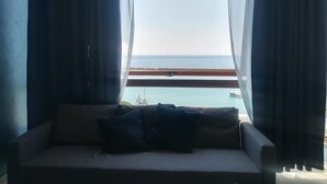 A room with a sofa facing a window overlooking a body of water and a distant shoreline. - Guest House Domus Cicerone (Formia)