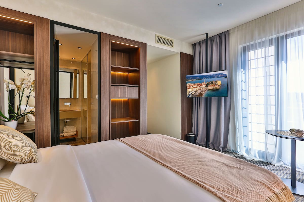 A hotel room with a large bed, a TV mounted on the wall, a small table, and a window with curtains.