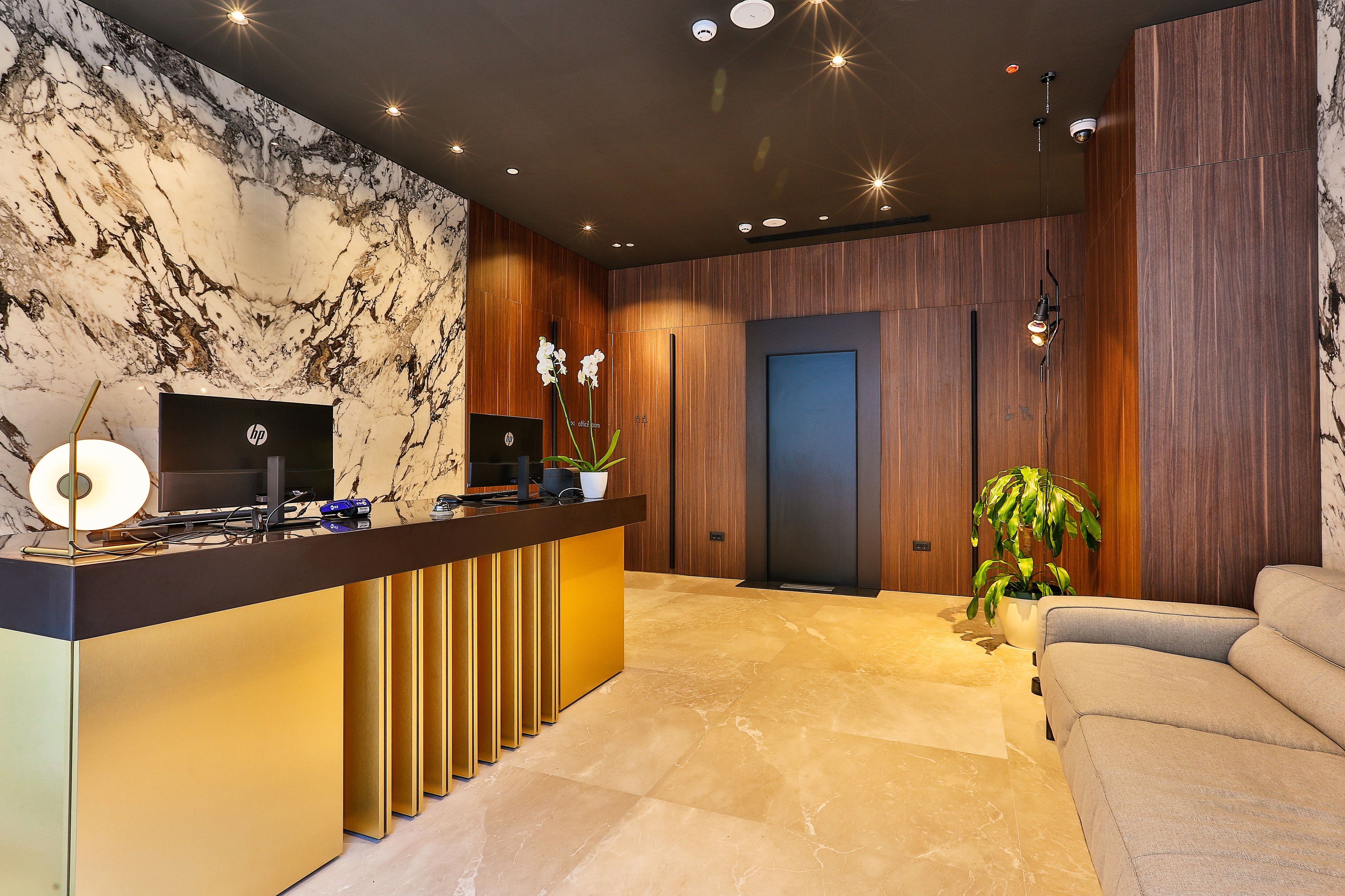 A modern reception area with a marble wall, a reception desk, a sofa, and a door.