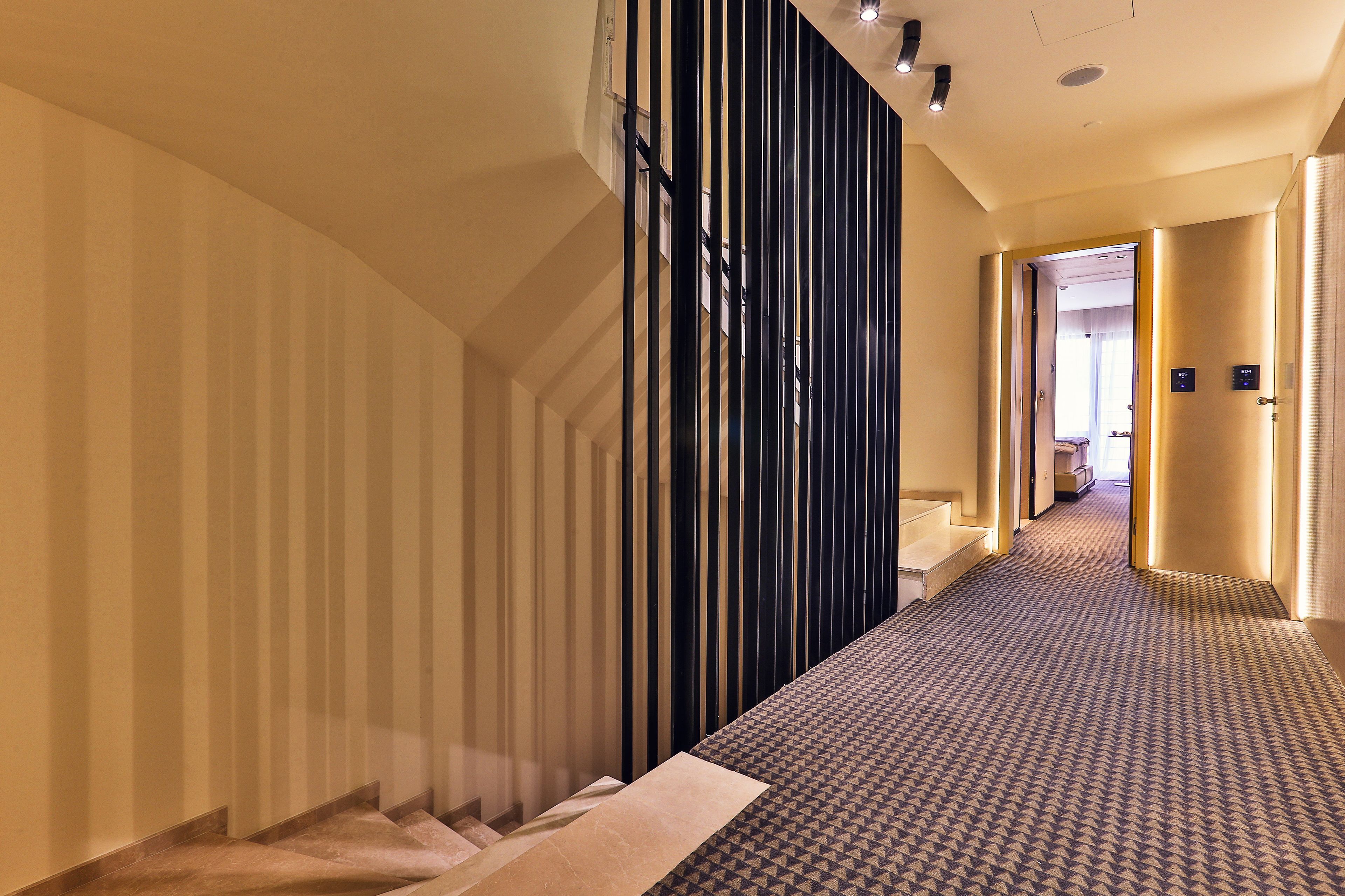 A hotel hallway with a patterned carpet, a staircase, and a modern design with vertical lines on the walls.