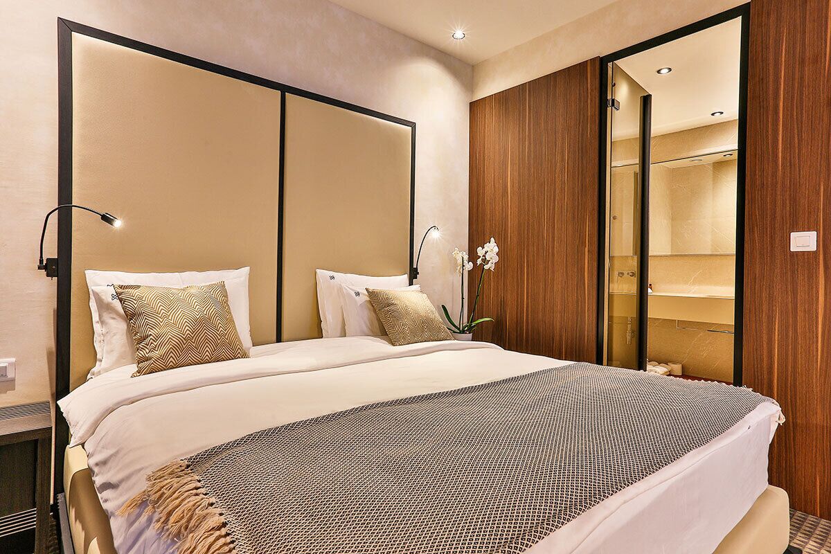 A hotel room with a large bed, a wooden wardrobe, and a mirror.