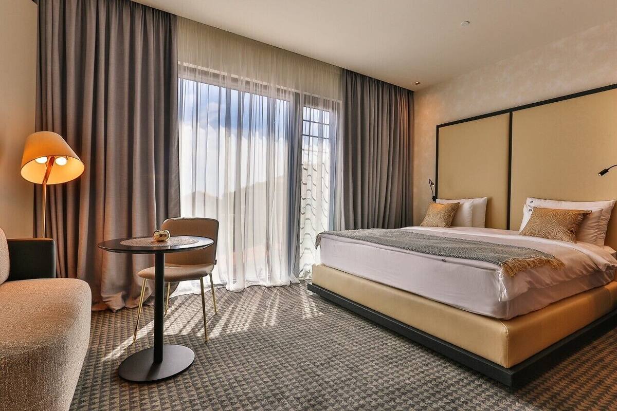 A hotel room with a bed, a chair, a small table, and a lamp.