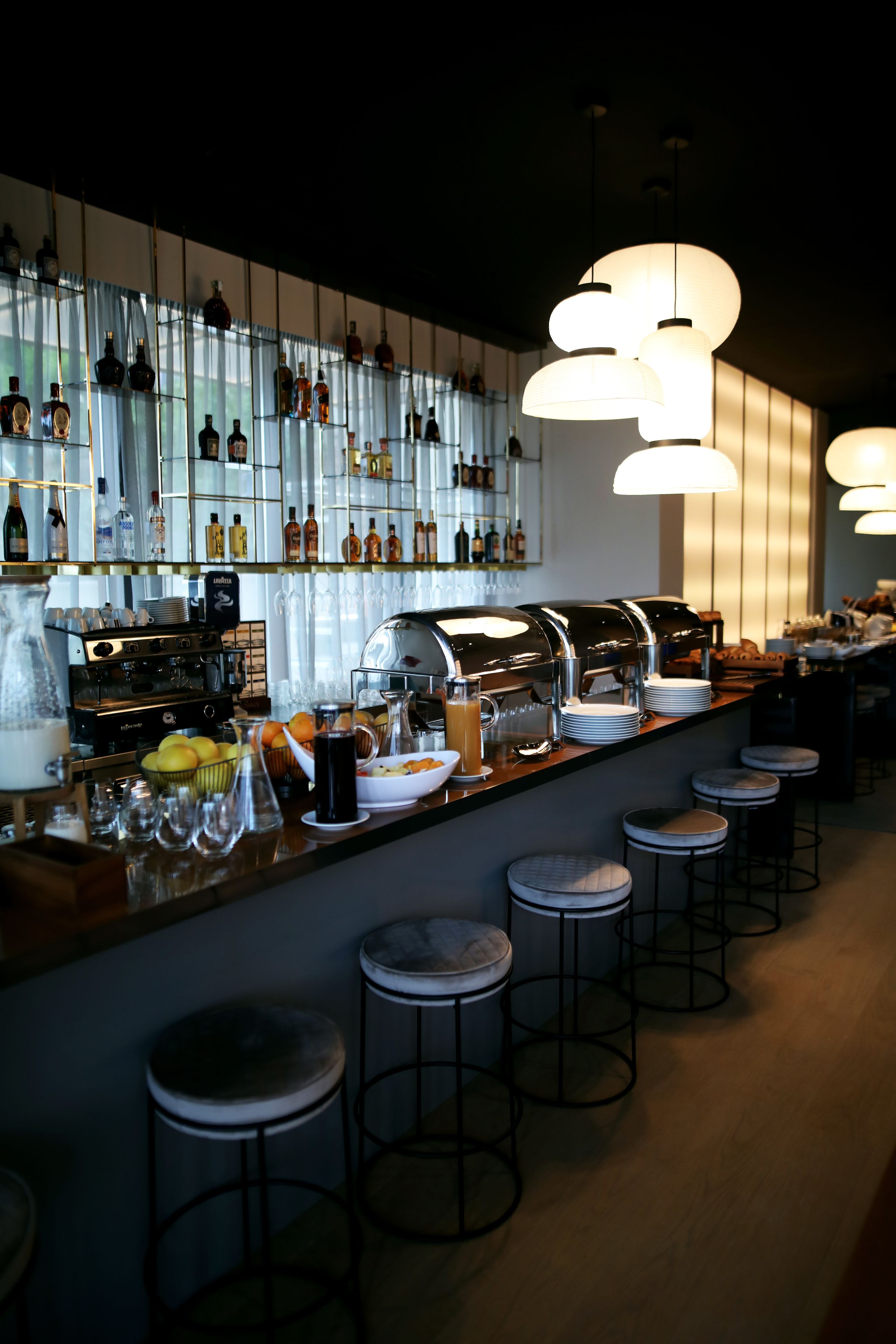 Un espace bar doté d’un long comptoir, de nombreux tabourets et d’une variété de bouteilles et de verres disposés sur des étagères.