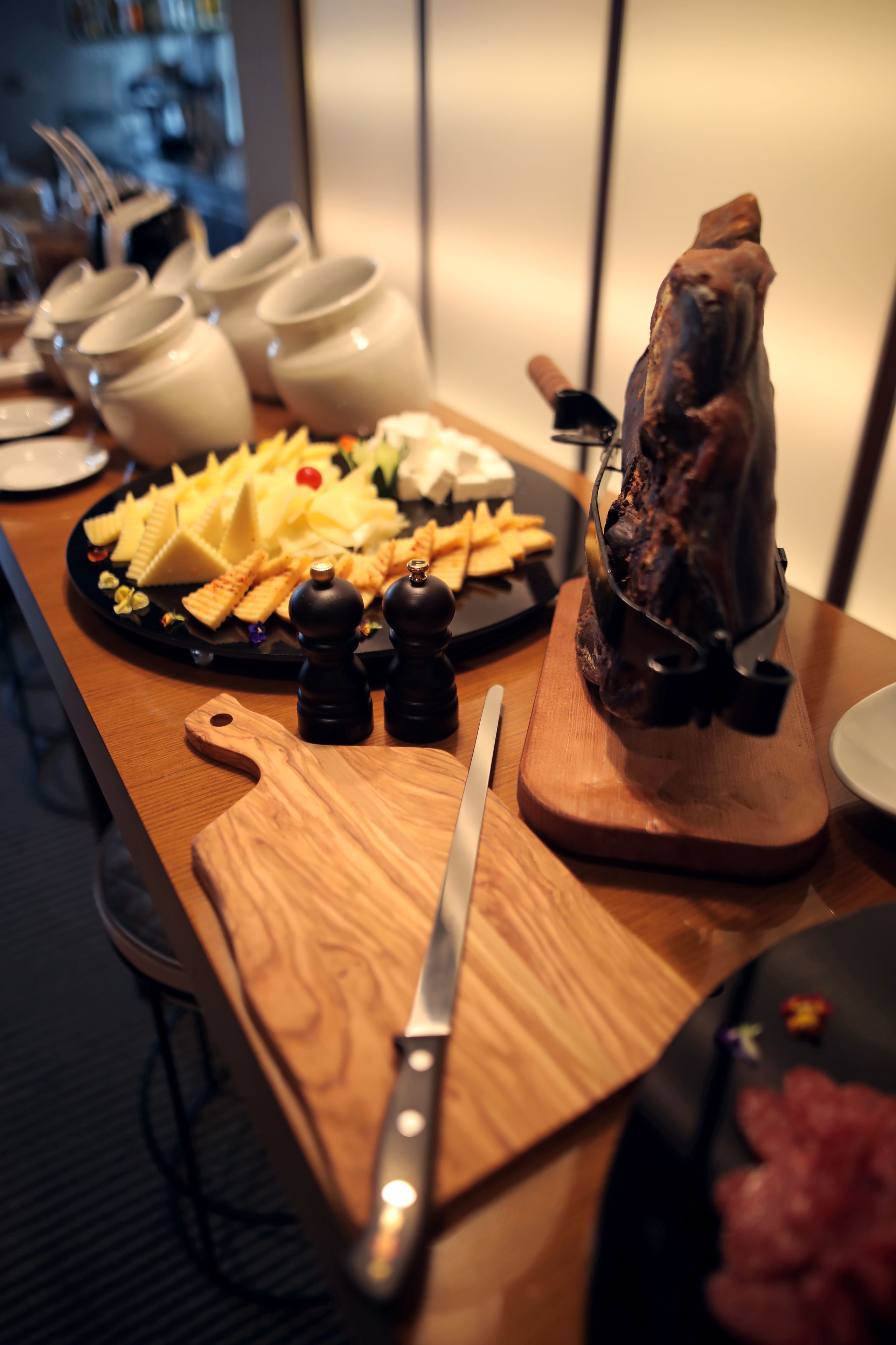 A wooden table with a cheese platter, a knife, salt and pepper shakers, and a meat carving stand.