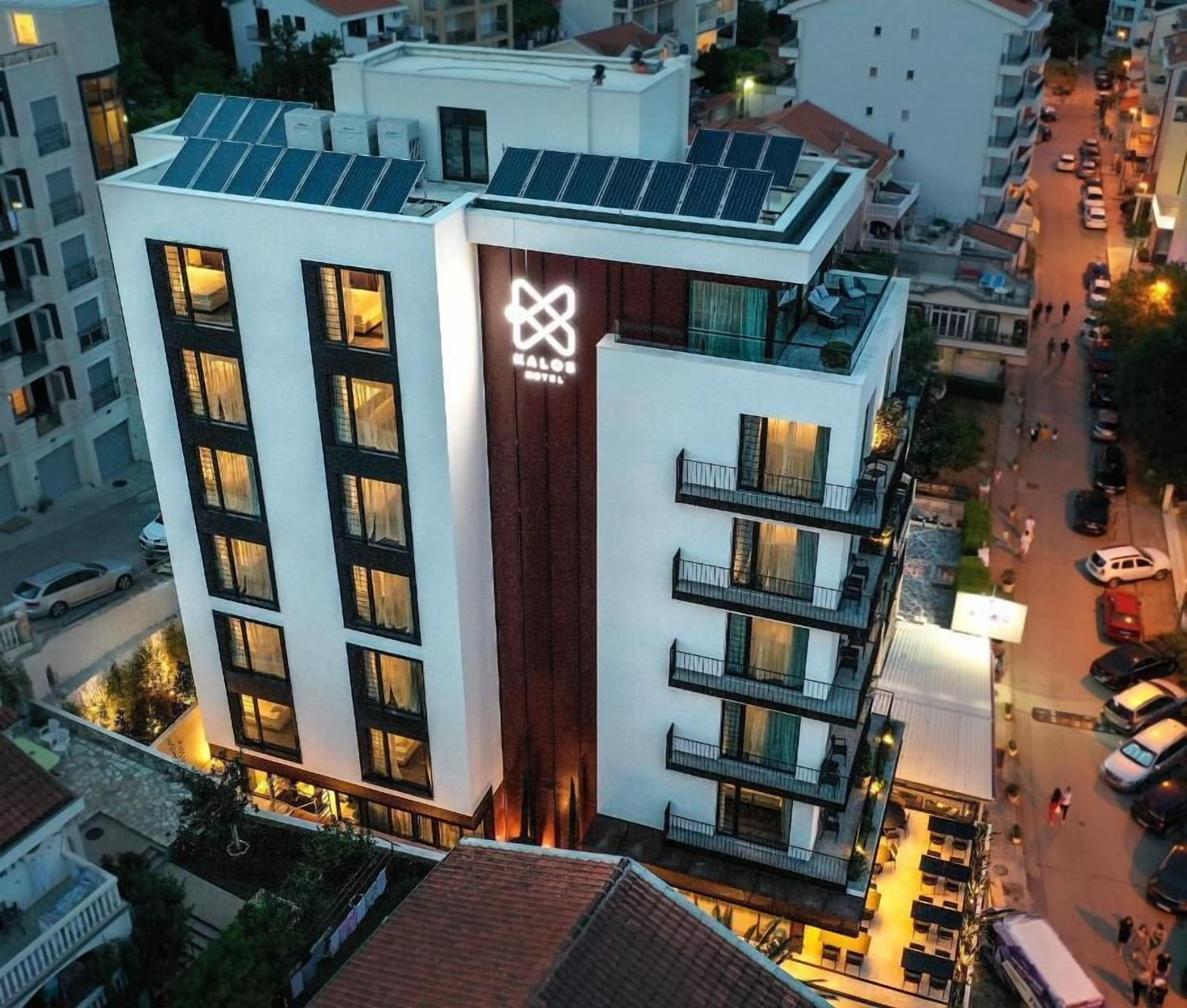 Un hotel moderno con un logotipo destacado, varios balcones y paneles solares en el techo.