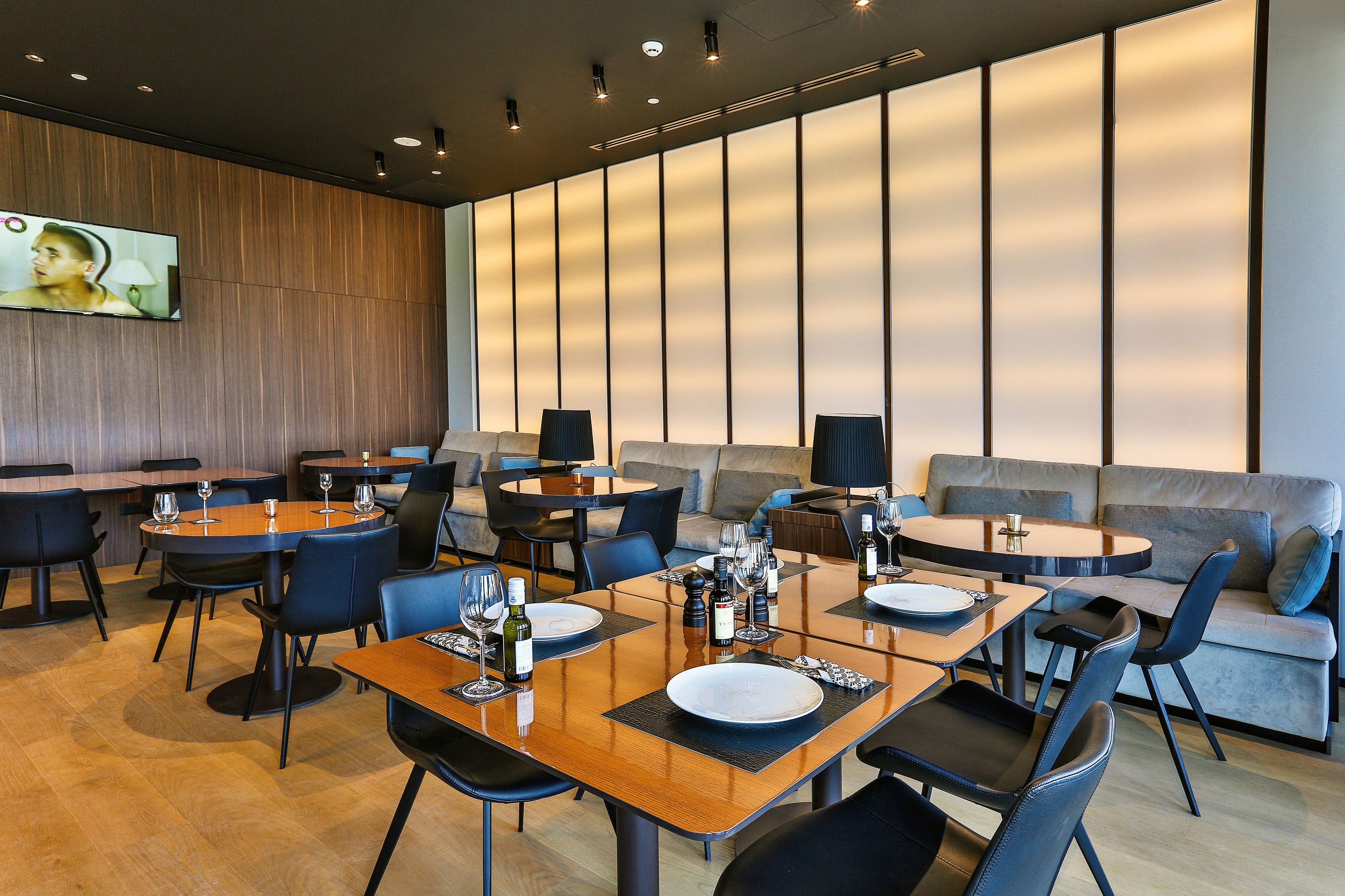 A modern restaurant with wooden tables, blue chairs, and a large wall with vertical panels.