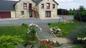 A two-story stone house with a red garage door, a red staircase, and a swing set in the yard. - Chambres d'Hotes Bel Air (La Selle-Craonnaise)