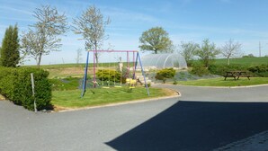 A park with a swing set, a picnic table, and a greenhouse. - Chambres d'Hotes Bel Air (La Selle-Craonnaise)