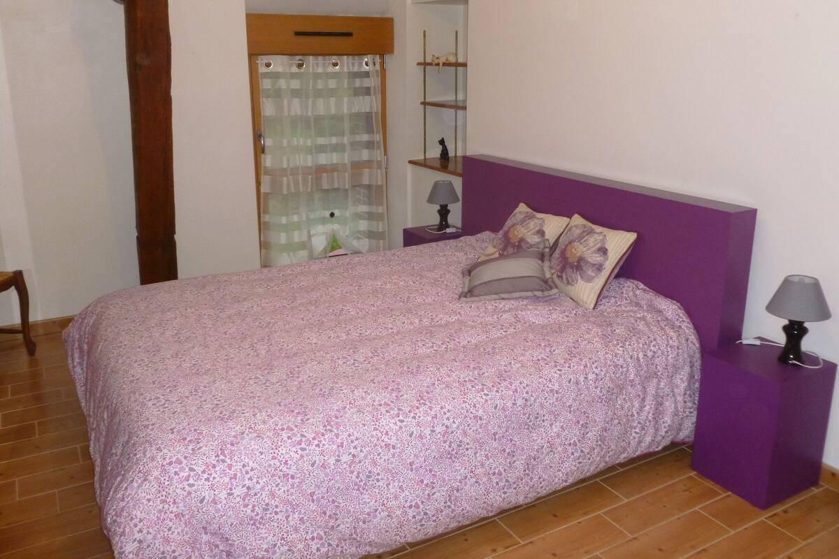 A bedroom with a bed, two nightstands, a chair, a wooden door, and a shelf with a cat.