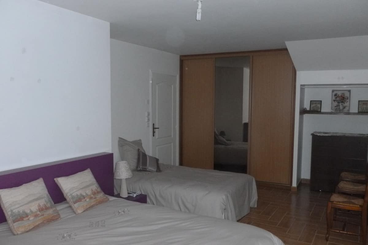 A bedroom with two beds, a wooden wardrobe, a chair, and a small table.